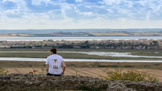 Havens to Havens Walk participant sitting on a hill looking out at the view. His race number and a photo of a loved one is pinned to the back of his t-shirt