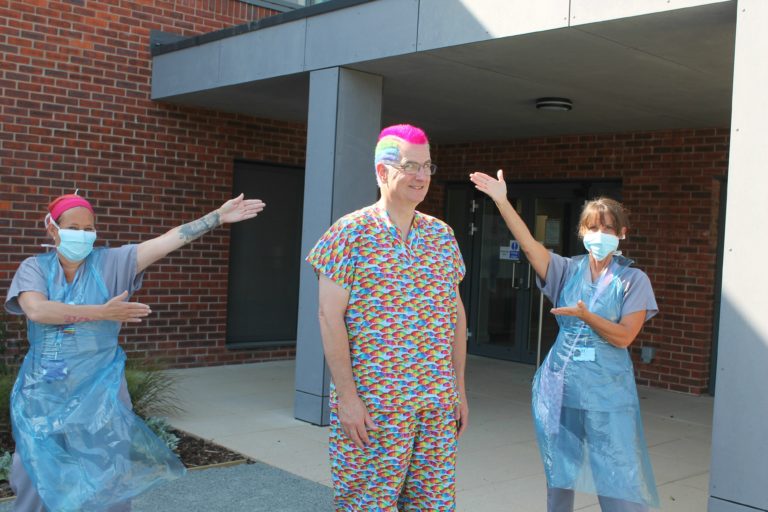 Dr Tosh outside the hospice with rainbow coloured hair and scrubs in a rainbow pattern