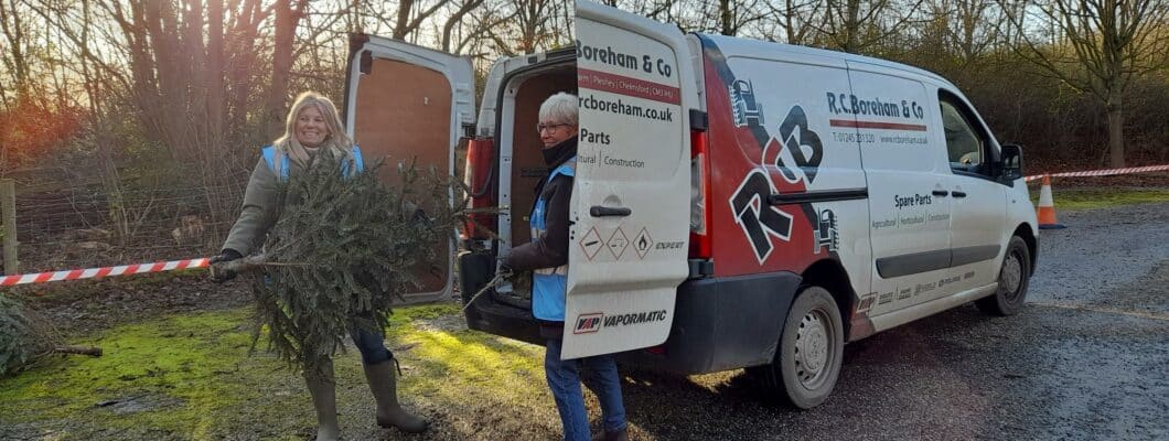 Two volunteers loading a christmas tree into the back of a van