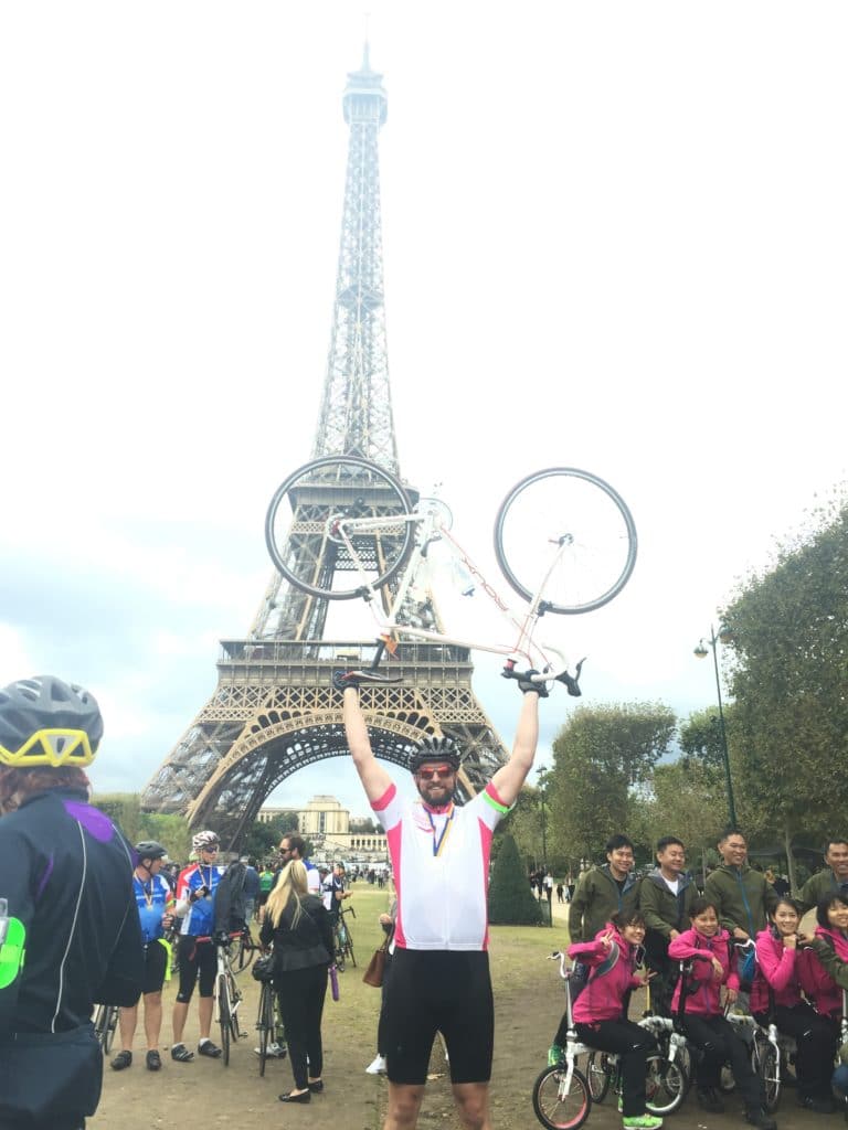 Trustee, Stewart Turner, holding his bike up in front of the Eiffel Tower after completing the London to Paris cycle in 2016