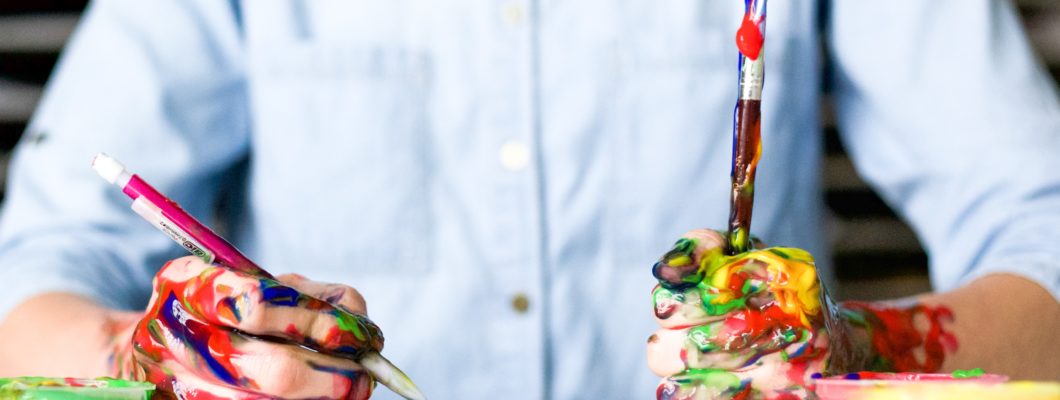 hands covered in paint holding paint brush