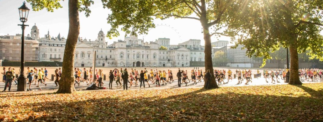 Photo of buckingham palace in the distant runners in front with leaves and trees in front of them