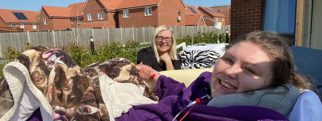 Lucy in bed outside hospice garden holding hands with her mum