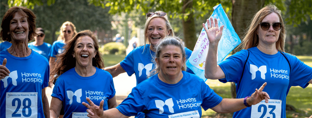 Group of four people waving at camera. Walking along wearing blue havens t-shits with white race numbers on their fronts