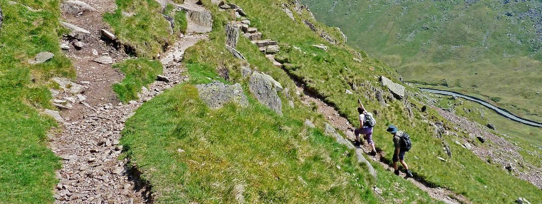 two hikers can be seen from a distance walking up green hills