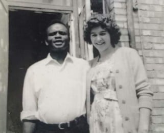 A black and white photo of a man and a woman standing in the doorway of a hosue