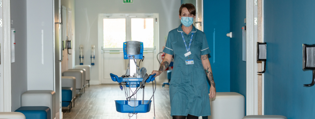 Fair Havens Nurse walking down corridor at the hospice with blood pressure machine