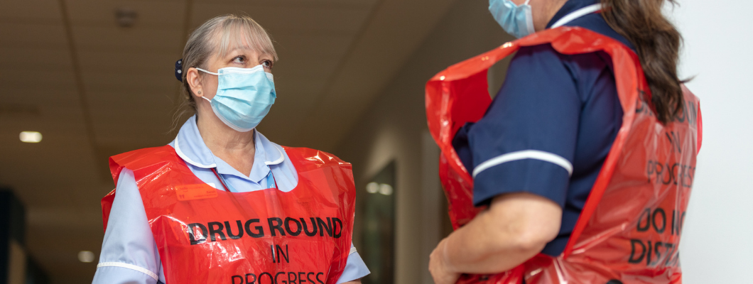 Nurse at Fair Havens wearing red drugs round apron talking to another nurse