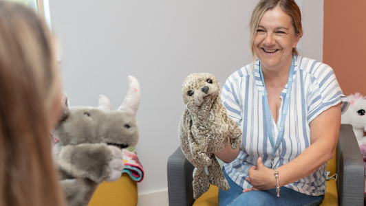 child counsellor playing with a puppet talking to a child, only can see the back of child's head in the photo