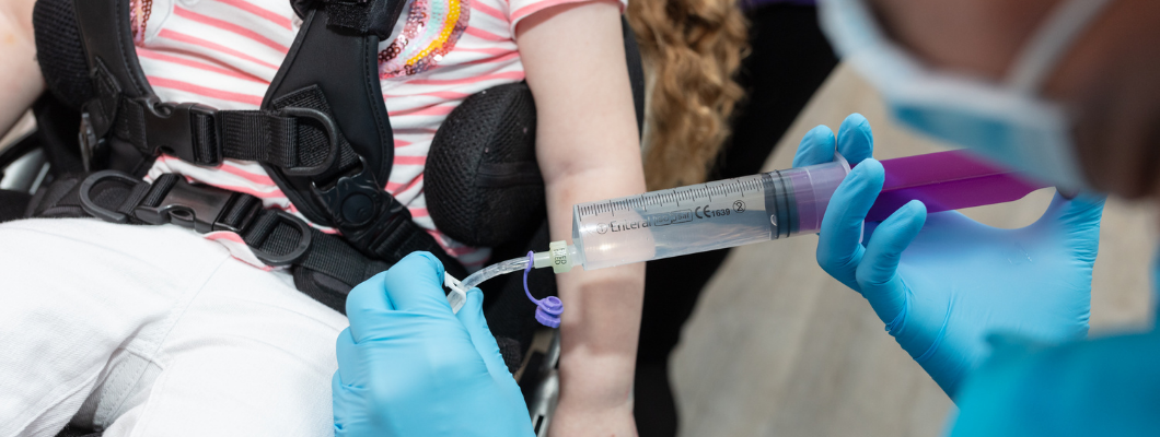 Nurse wearing blue gloves administering medication to a tube into child's stomach