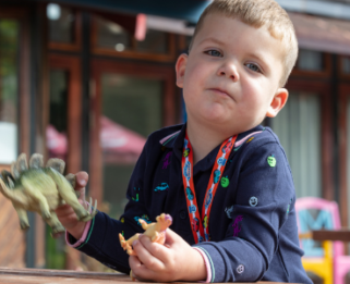 Boy sat in garden at Little Havens playing with dinosaur toys