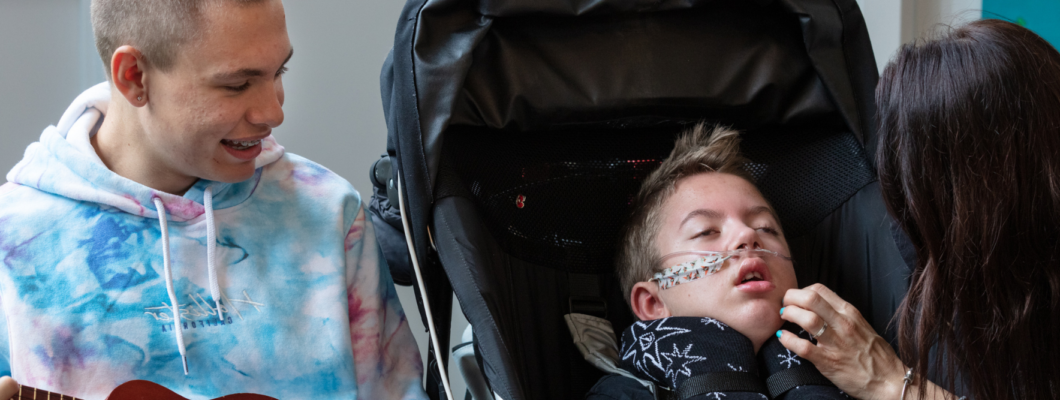 boy sat in wheelchair with brother next to him smiling and mum touching his face