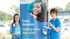 two people wearing havens blue tops by tall banner holding bucket collections