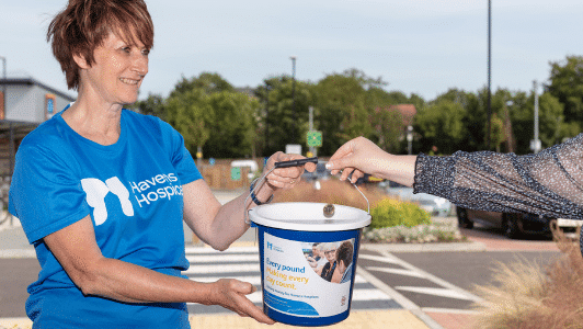 fundraiser wearing blue havens hospices top holding bucket with hand putting pound coin into it