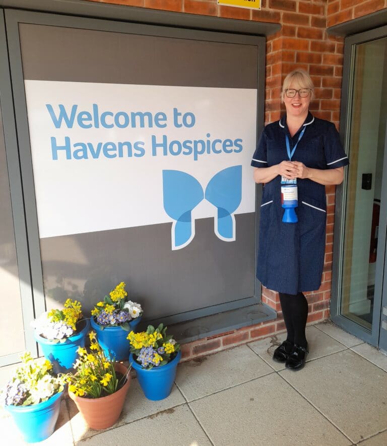 Lady in Nurse uniform standing outside hospice with collection tin