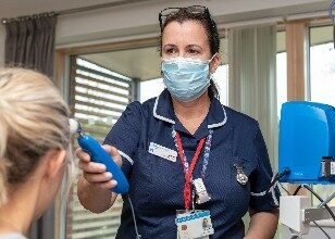 Nurse at Fair Havens wearing mask taking patients temperature