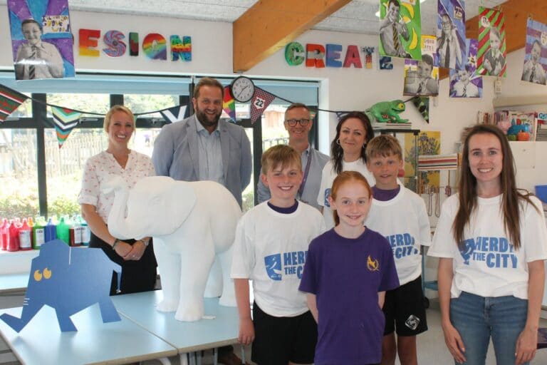 A group of adults and children pose for the camera with a baby elephant statue