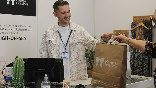 Young man stood behind the till passing over a brown paper bag to a hand that is stretched out