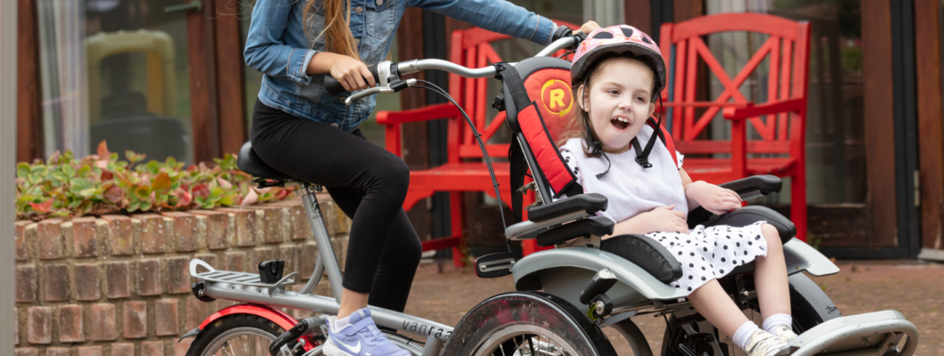 Rosie sat on the front seat of a trike smiling as someone pedals behind her