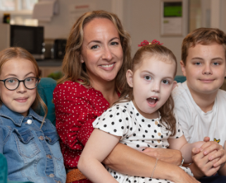 Rosie sat on her mum's lap with brother and sister sat either side smiling at the camera