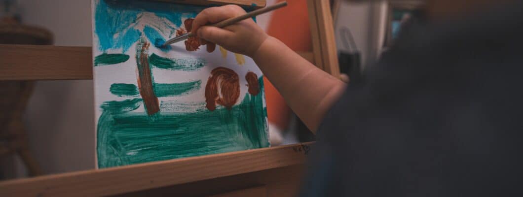 Hand of a child painting a garden scene on a small easel in front of them