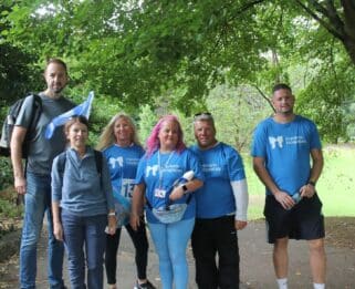 Six people standing outside in woods looking to camera, four wearing blue t shorts with havens butterfly logo
