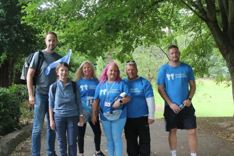 Six people standing outside in woods looking to camera, four wearing blue t shorts with havens butterfly logo
