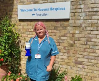 Abbi in her nursing uniform holding a collection tin outside Little Havens Hospice