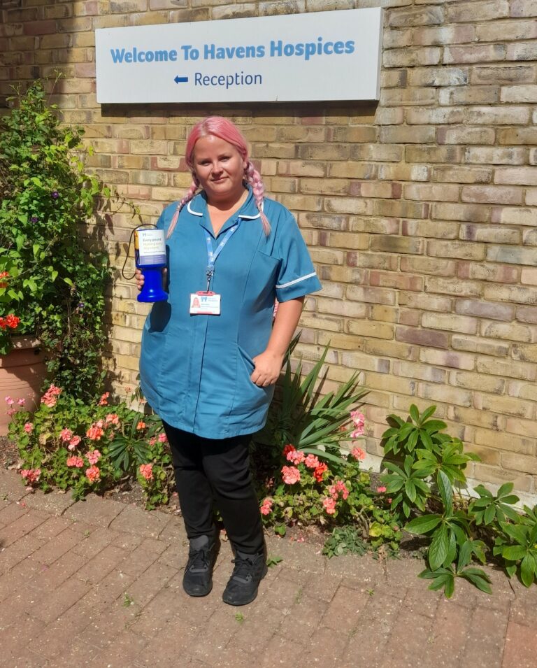 Abbi in her nursing uniform holding a collection tin outside Little Havens Hospice