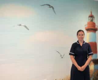 Pamela Houghton-Clarke standing in front of a lighthouse wallpaper mural