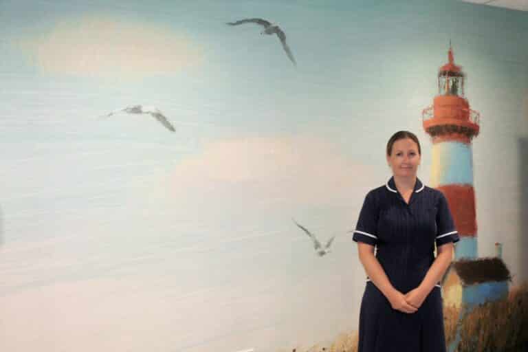 Pamela Houghton-Clarke standing in front of a lighthouse wallpaper mural