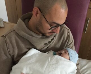 Aron hugging, Evan, a baby wrapped in a white blanket