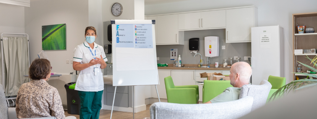 Occupational therapist stood talking to the room with two patients sat in the chair in the room