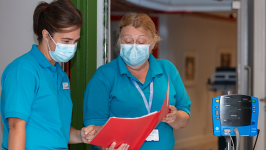 two nurses at Little Havens wearing masks discussing medication in the corridor