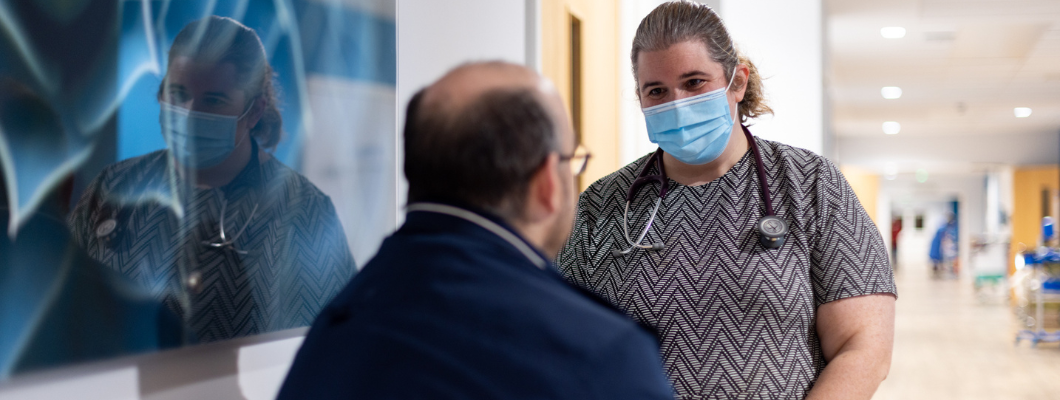 Doctor wearing a stethoscope talking to a relative sat outside a room, you can only see the back of the relative's head