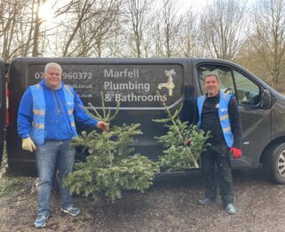 Two volunteers holding real Christmas trees next to their company's van