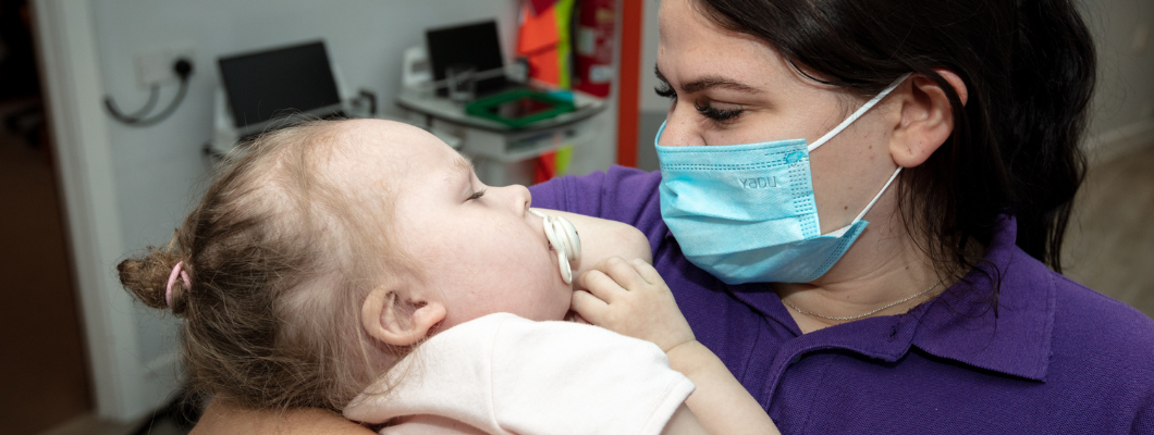 young child asleep in arms of care team member who is wearing a mask and looking at her