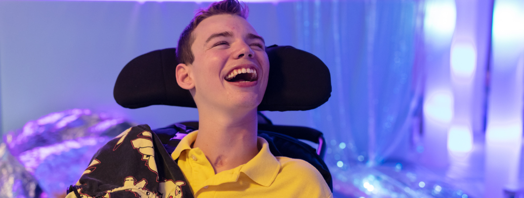 Teenage boy laughing with his mouth open, behind him is blue sensory lights on the wall