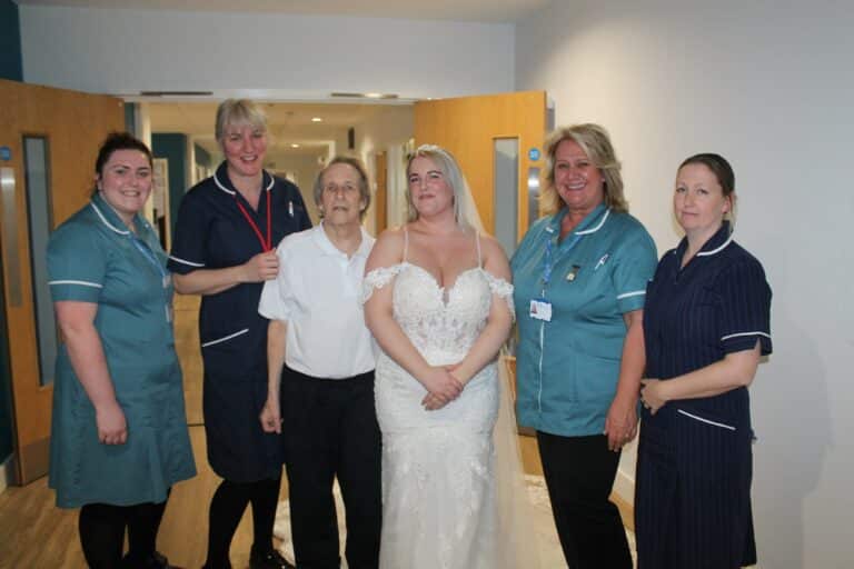 Richard Bailey with Emily Bailey in a wedding dress standing with four members of the Fair Havens Care Team