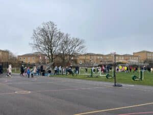 Several children and parents running around a playground and field