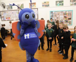 Blue butterfly mascot, Betsy, with children in a school hall