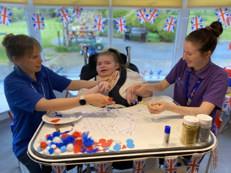 Two members of staff at Little Havens assisting a child patient with her craft activity