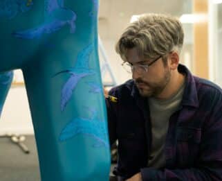 Man leaning down writing with a posca pen on an elephant sculpture