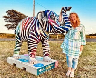 Jenny Sexton standing next to 'Living the Dream' elephant, decorated as a zebra in bright colours