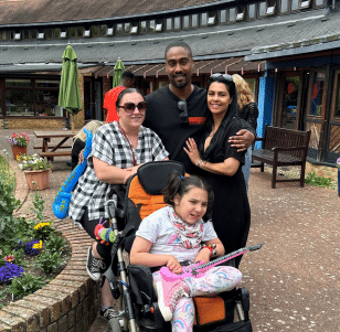 Simon Webbe and his wife stood outside with a mum and a teenage girl in her wheelchair with her leg crossed
