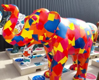 A vinyl patchwork elephant in blue, yellow, red and pink standing on a concrete plinth