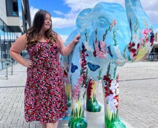 Charlie Stafford standing next to a decorated elephant sculpture painted with wild flowers and butterflies