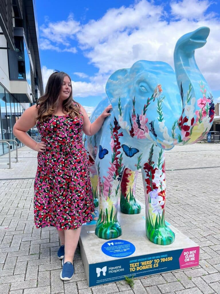 Charlie Stafford standing next to a decorated elephant sculpture painted with wild flowers and butterflies