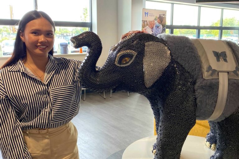 Kaye Mercene standing next to a baby elephant sculpture covered in silver and grey nuts and bolts