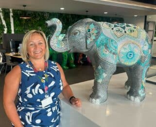 Sarah Nash standing next to a baby elephant sculpture covered in thousands of sparkly rhinestones